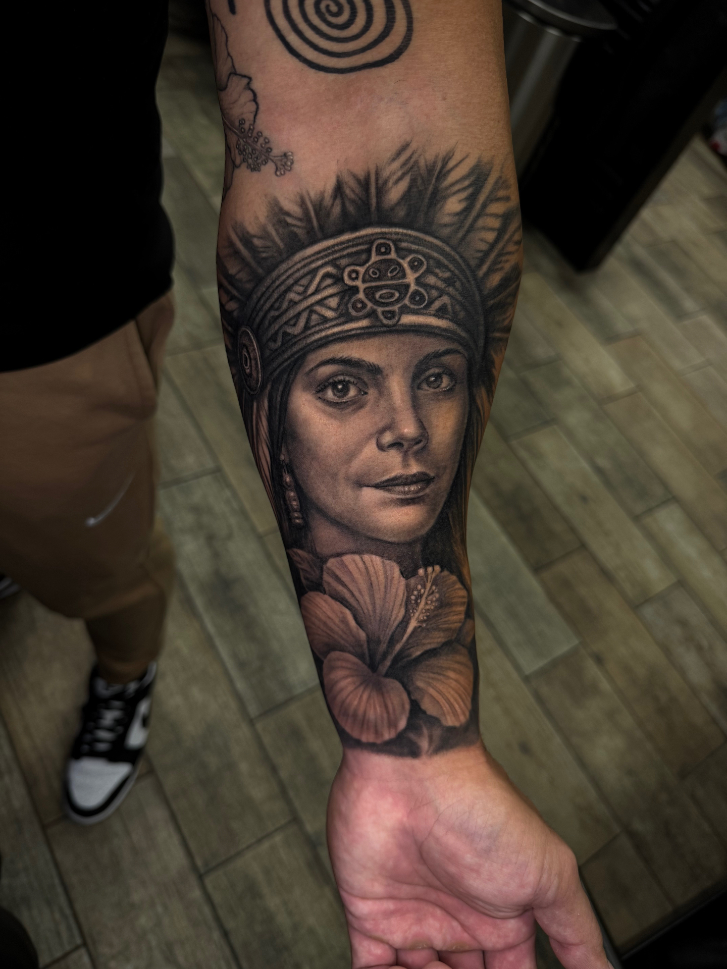 Black and grey portrait tattoo of an indigenous woman with floral details on the forearm